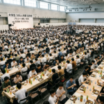 Hundreds of university students seated at long tables eating lunch in a large hall during an alcohol-free event